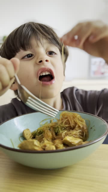 Young Boy Lunchs on Chicken and Broccoli Pasta in a Bowl During Lunch, Using a Fork