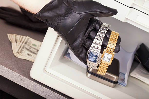 The gloved hand of a thief who is stealing watches and cash from a safe.