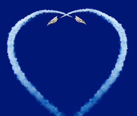two paper planes leaving a heart shaped vapour trail