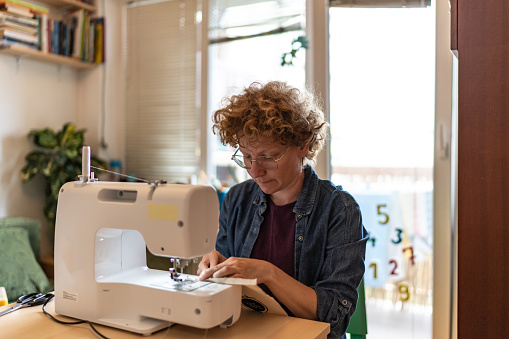 Woman using sewing machine at home. Small business