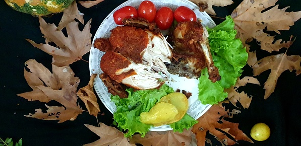 A white plate with a grilled chicken breast and salad garnished with lettuce, tomatoes and slices of lemon