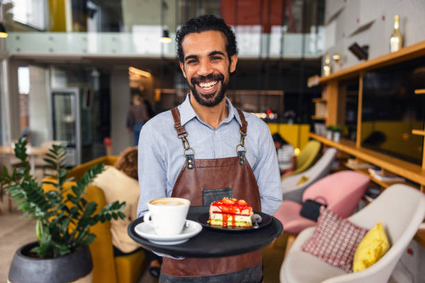 istock Cheerful Male Bartender Smiling At The Camera While Holding A Drink Tray In A Colourful Cosy Cafe 1761309919
