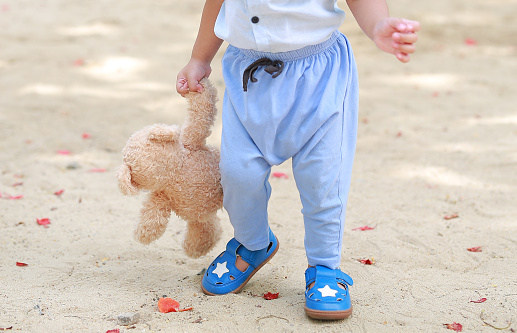 Close-up baby boy walking with holding teddy bear in the garden outdoor.