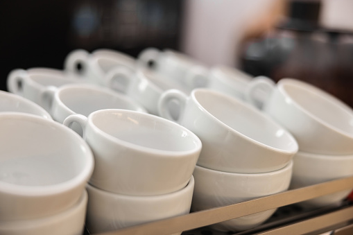 Close up of simple and minimalistic white coffee cups stacked on a rack in a coffee shop.