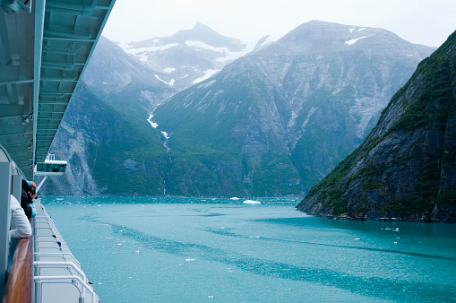 Near vertical mountain slopes carved by glaciers. The cold blue green waters of Tracy Arm Fjord in Alaska as viewed from a cruise ship.