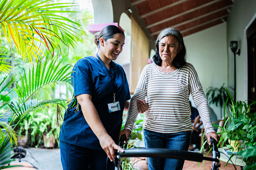 Home caregiver helping senior woman to walk at nursing home