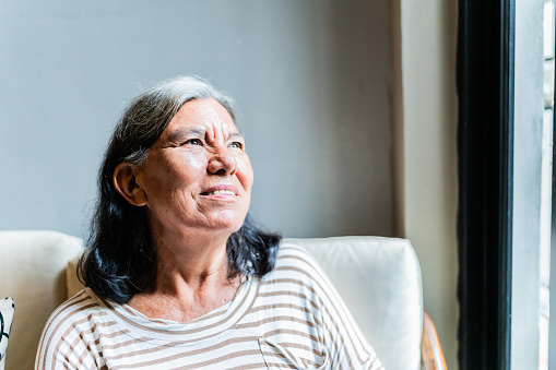 Senior woman contemplating and looking through window at home