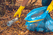 A woman fights to save the forest from garbage. A woman with a garbage bag in her hands collects plastic waste in the forest. Ecology, saving nature from plastic waste.