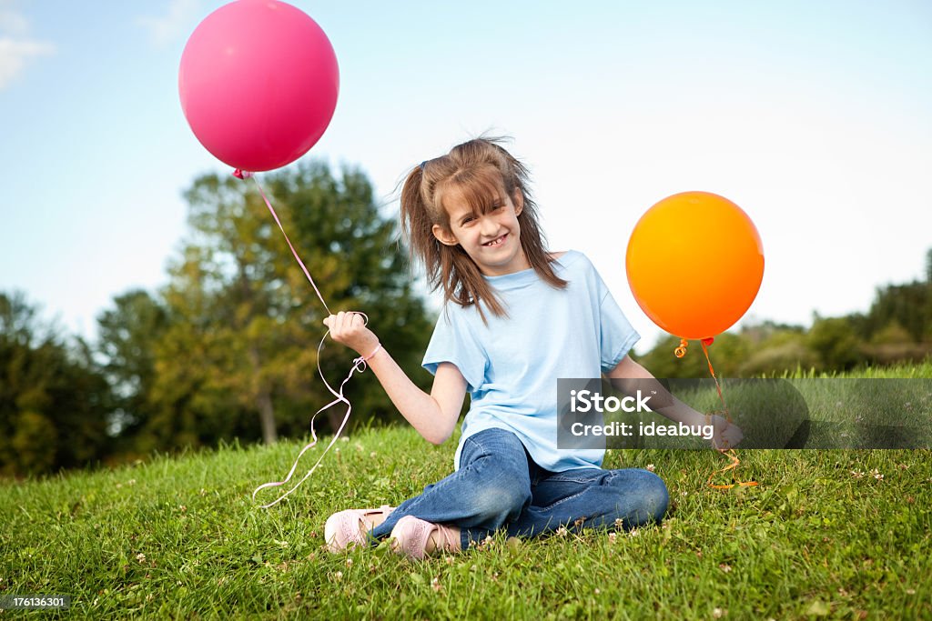 Chica joven sentado en el césped y sujeta los globos - Foto de stock de 8-9 años libre de derechos