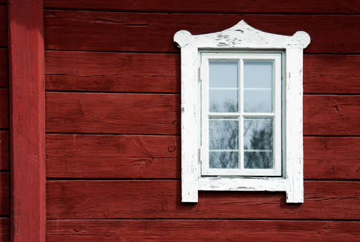 Three old windows with grilles and carved wooden green-white architraves on red wall from board.Facade of typical house of Nizhny Novgorod province, Russia, built in 19th century. Architecture concept