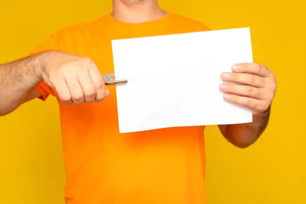 Half-length portrait of a man holding a blank sheet with a hole-punching device, isolated on yellow studio background