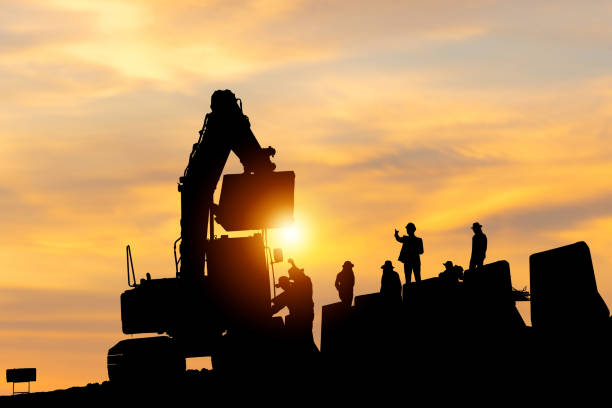 istock Silhouette of Engineer and worker checking project at building site, Engineer and builders in hardhats discussing on infrastructure construction site sunset in evening time background 1761371482