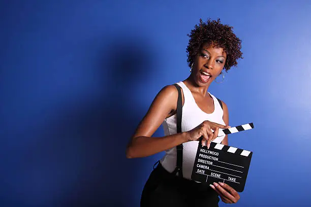 Beautiful young woman holding a clapboard and shouting ACTION!