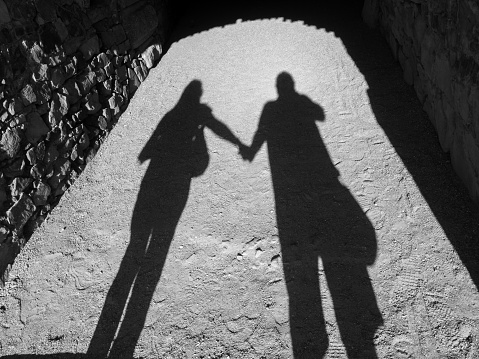 Black and white photograph of the shadow of a couple holding hands. Love concept.