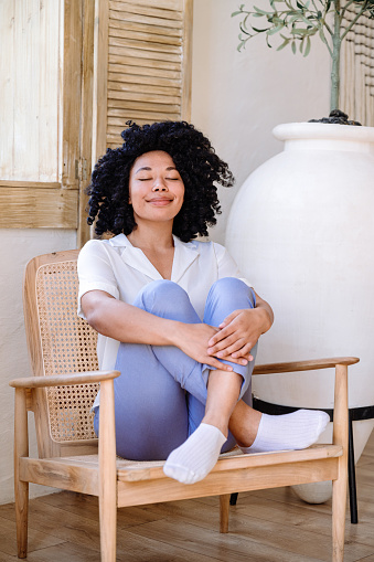 positive peaceful african american woman resting on chair in cozy living room, enjoying break and dreaming with closed eyes. visualization concept