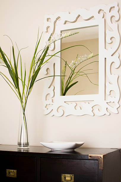 Round mirror with metal frame sitting on two artificial plants