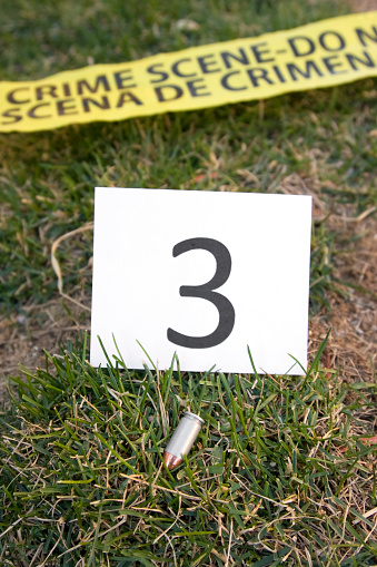 A crime scene with a bullet, crime scene tape and an evidence marker.