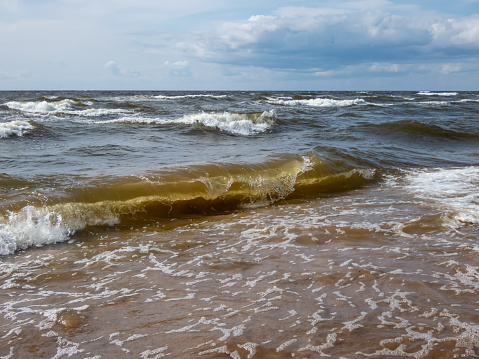 Beautiful outdoor scenery of seascape of the Baltic sea with big foamy waves in windy day with brown sand on the shore and blue sky above