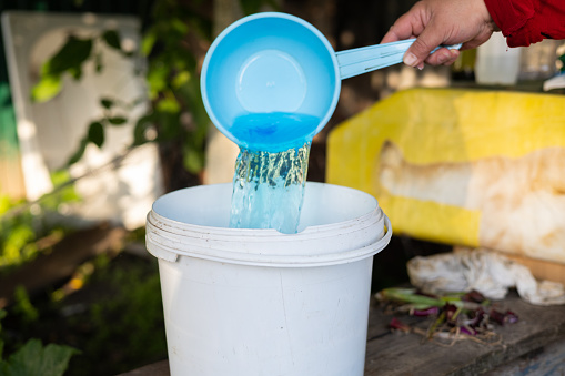 In the garden a woman mixes a fertilizer solution in a bucket to feed the plants A woman prepares an aqueous solution of fertilizers to feed vegetables in the garden. Fertilizer concept in gardening.