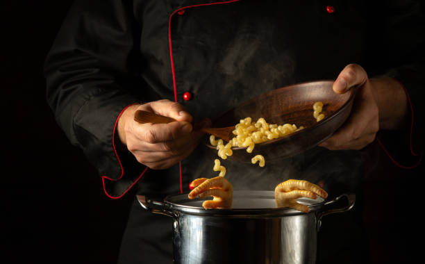 Adding pasta with the chef hands to a pot of boiling chicken legs. Concept of preparing delicious soup in the kitchen of a restaurant or hotel