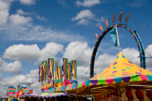 A colorful carnival midway against a beautiful cloud filled blue morning sky.  Plenty of room for copy.