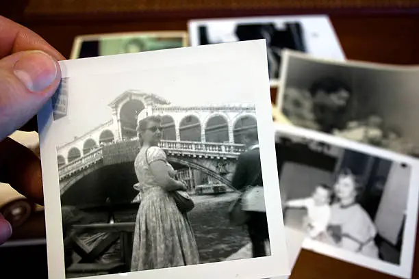 Hand holds vintage photograph of female traveler with pile of old photos in background.  Please view my