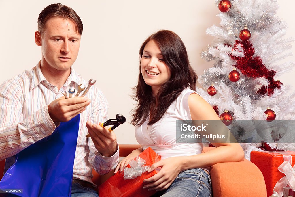 young couple exchanging christmas gifts (series) a young couple is sitting on the couch and exchanging christmas gifts. he doesn't seem to be very happy about his new toolset and all the repairs he is supposed to do with them. Gift Stock Photo