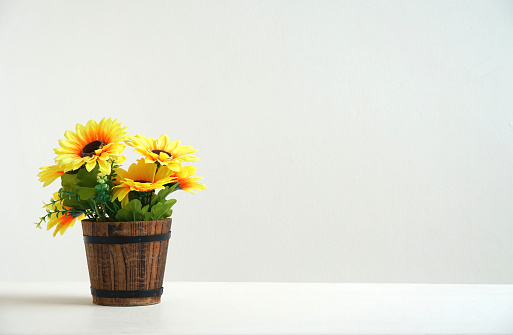 artificial sunflower In a pot made from colored wood. Place the decorations on the white table. There is a blank white wall as the background for adding content.