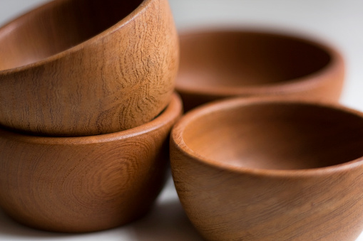 A DSLR photo close up studio shot of 4 wooden bowls handmade. There is a pile of two at the left side and one behind the other on the right side. 