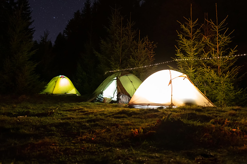 Evening at a camping in the mountains. Illuminated tents in a picturesque valley.