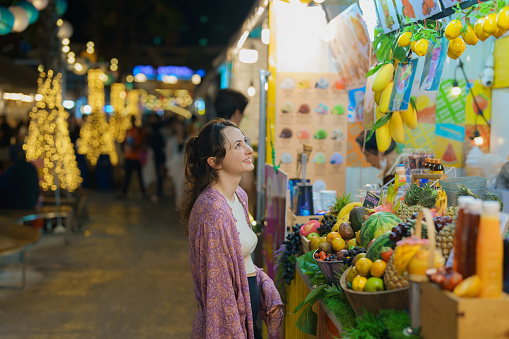 Cheerful woman ordering smoothie on  night market in Bangkok, Thailand