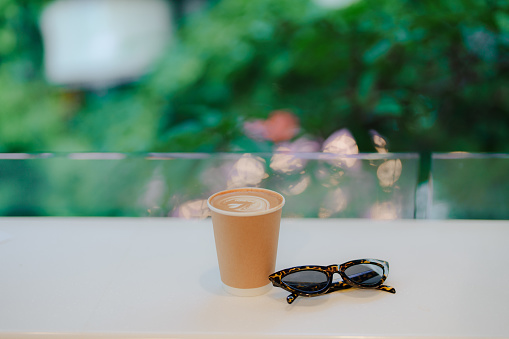 Coffee in paper cup and sunglasses on white table with view