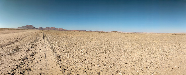 Panorama of a barren agricultural field with a very thin fence at the foot of mountains in the Namib-Naukluft National Park, Namibia