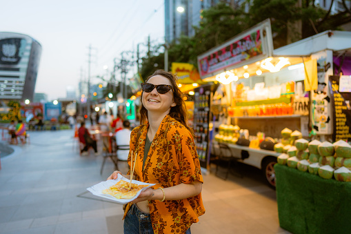 Cheerful woman eating thai pancakes (roti) on night market in Bangkok