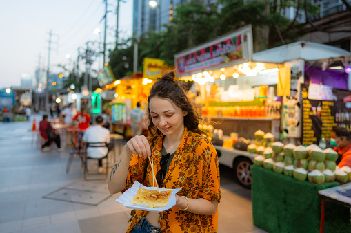Cheerful woman eating thai pancakes (roti) on night market in Bangkok