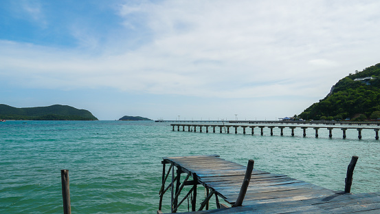 wooden bridge juts out into of the sea. Wooden bridge on the way to the harbor. Beautiful landscape. boardwalk to the horizon, turquoise water and blue sky with clouds.