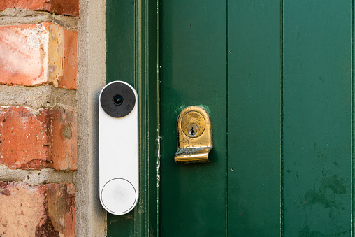 A video doorbell on a green door with a brass lock, on the door of a rural cottage, Northern Ireland