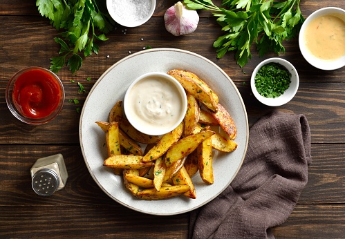 Baked potato wedges with sauce over wooden background. Top view, flat lay