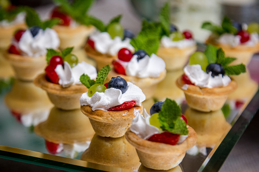 Tartlets with berries and whipped cream on a glass stand.