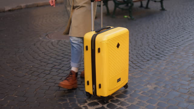An unrecognizable woman walking with a yellow suitcase on the European city street in the autumn