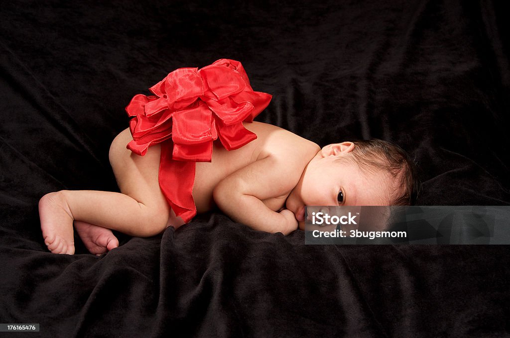 Newborn Baby with Red Christmas Bow on Black Background An adorable three week old baby lying on a black velvet blanket with a big red Christmas bow on her back.Find More Christmas Kids here Baby - Human Age Stock Photo