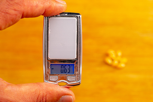 small precision weighing device on a hundredth scale held between the fingers of one hand