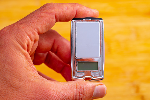 small precision weighing device on a hundredth scale held between the fingers of one hand