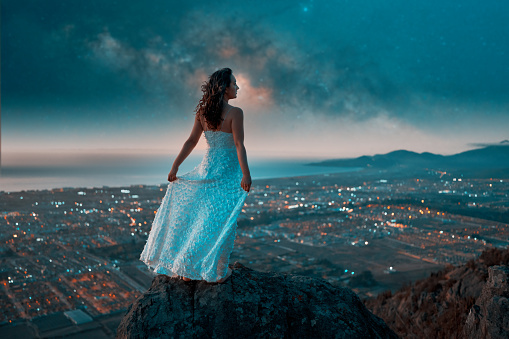 portrait beautiful woman on top of a hill posing with milky way and stars over the city
