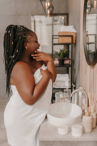 istock Confident plus size African woman touching face and radiating self-love while looking at the mirror in bathroom 1761707862