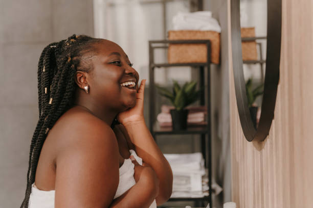 Happy plus size African woman radiating self-love while looking at the mirror in domestic bathroom