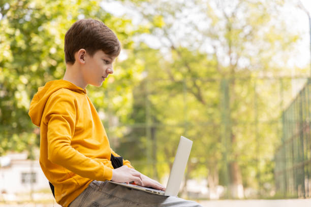 istock Thoughtful teenager boy resting. Holding and using a laptop for networking on a sunny day, outdoors. 1761716528