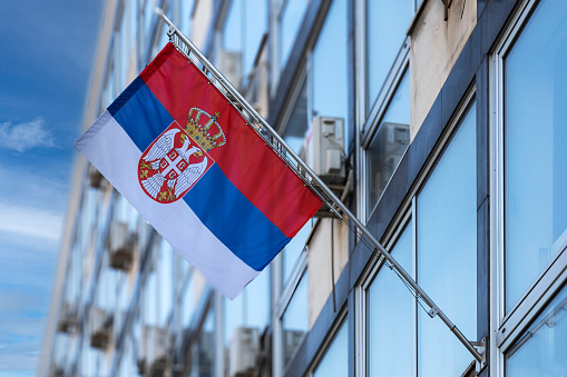 Serbian National Flag stretched on a flagpole placed on the facade of an administrative building.