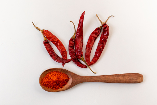 Dry red chili peppers and red chilli powder on wooden spoon kept on white background.