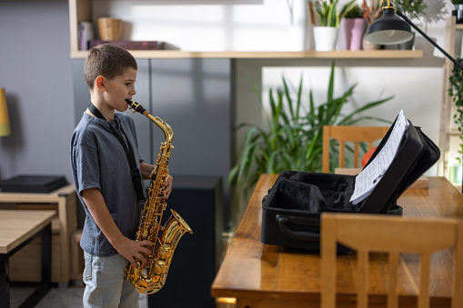 Young boy future musician practicing playing saxophone at home.
